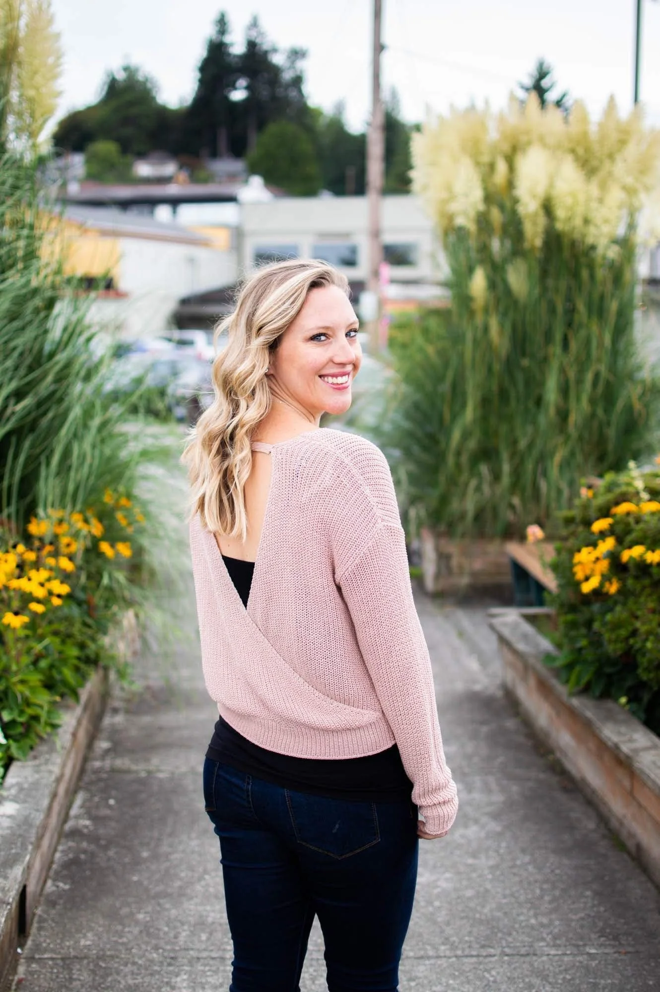 Mary Allison Jensen, LICSW, founder of A Legacy of Healing, smiling over her shoulder outdoors among flowers in a pink sweater — connect with a women's wellness educator and conscious self-leadership advocate.