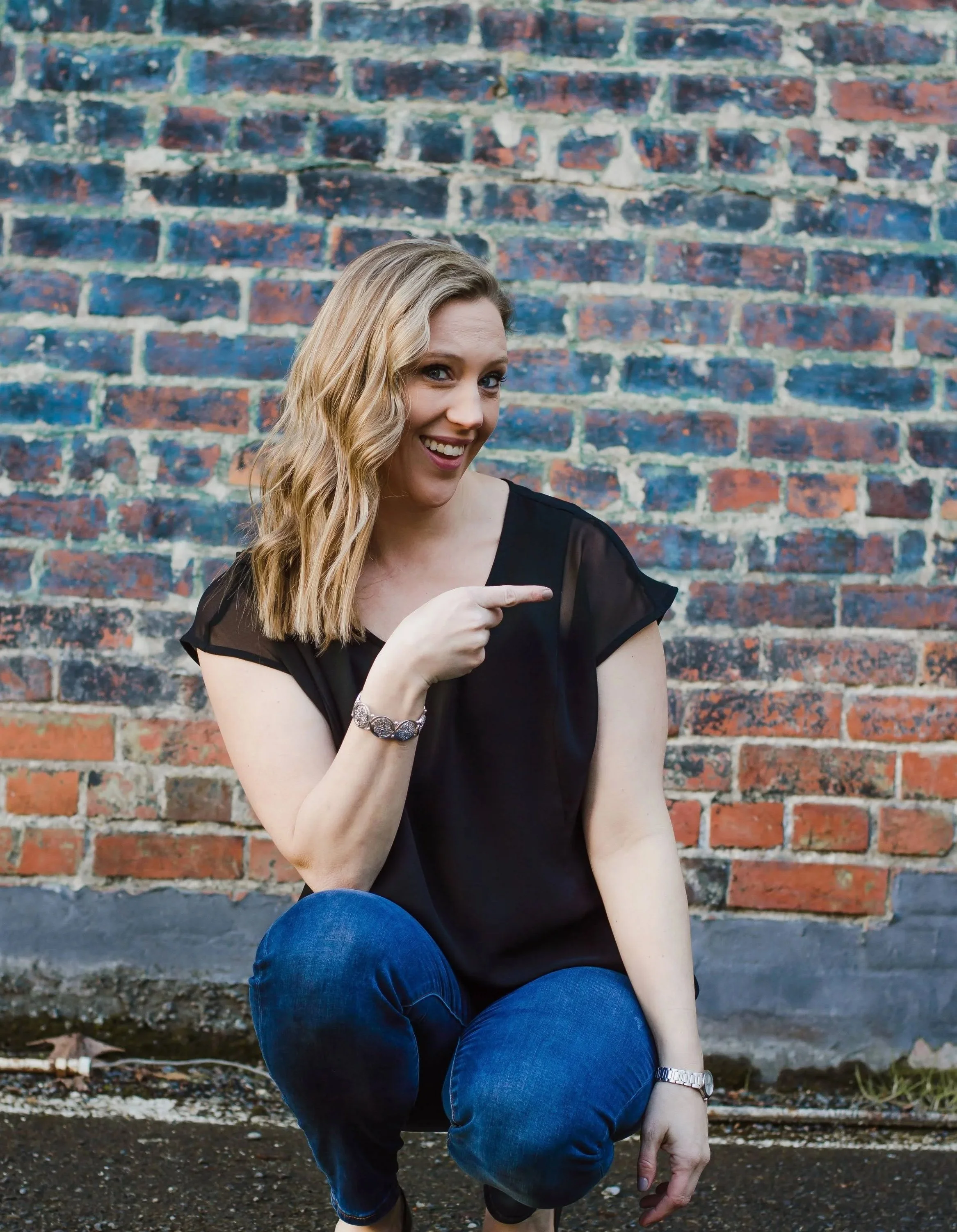 Mary Allison Jensen, LICSW, founder of A Legacy of Healing, smiling and pointing against a brick wall - licensed clinical social worker, generational healing architect, and mentor for women moving from self-abandonment to conscious self-leadership
