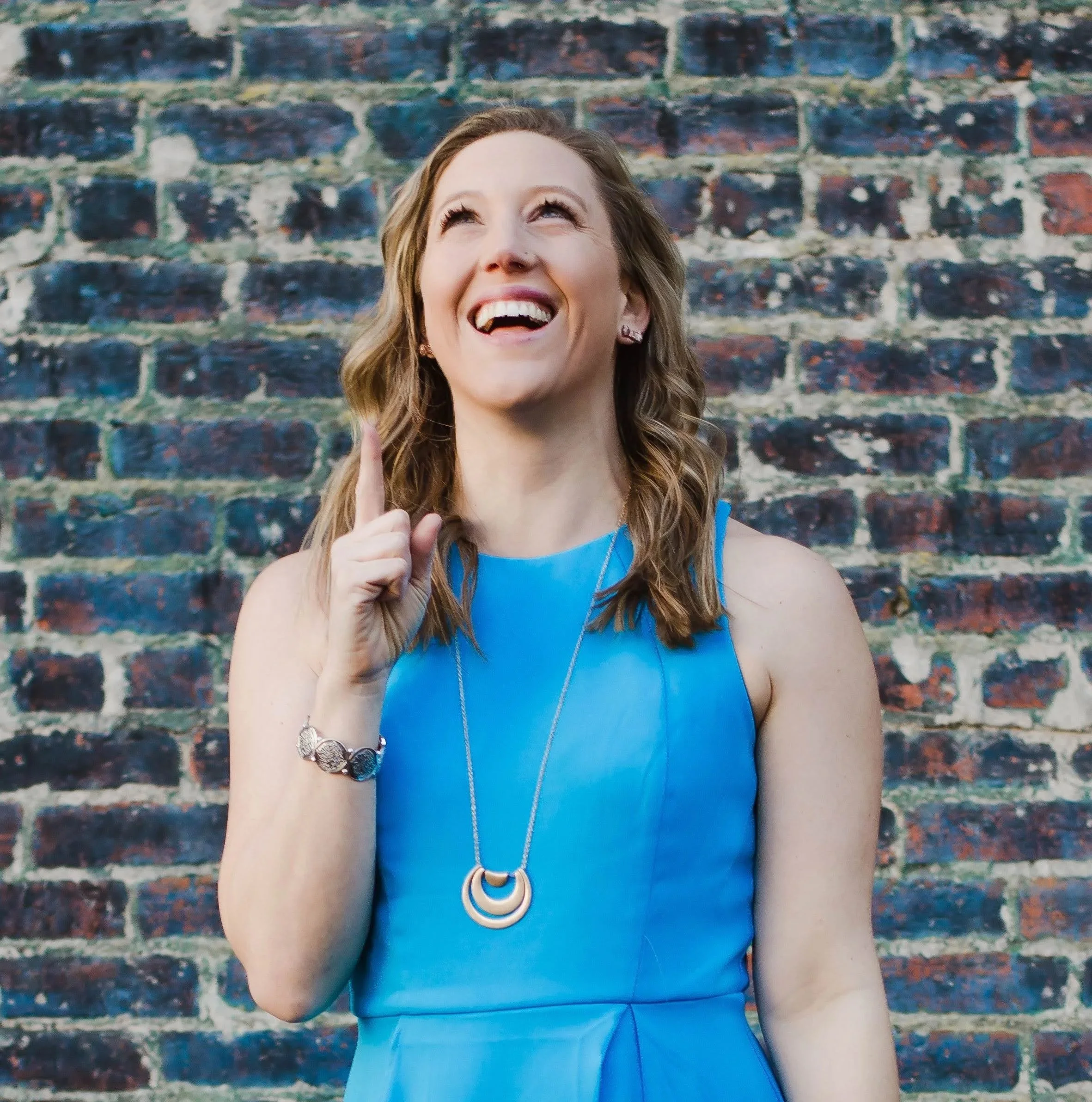 Mary Allison Jensen, LICSW, laughing joyfully in a blue dress against a brick wall — founder of A Legacy of Healing and creator of The Self-Love Lab.
