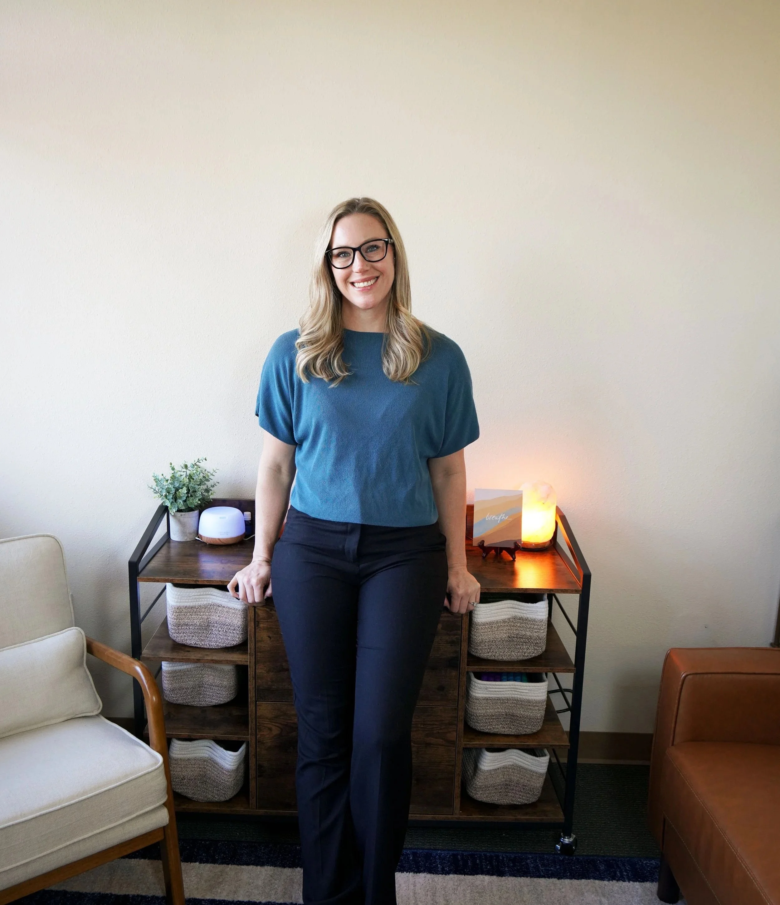 Mary Allison Jensen, LICSW, founder of A Legacy of Healing, smiling in a teal top and glasses in a warm, welcoming wellness office setting.