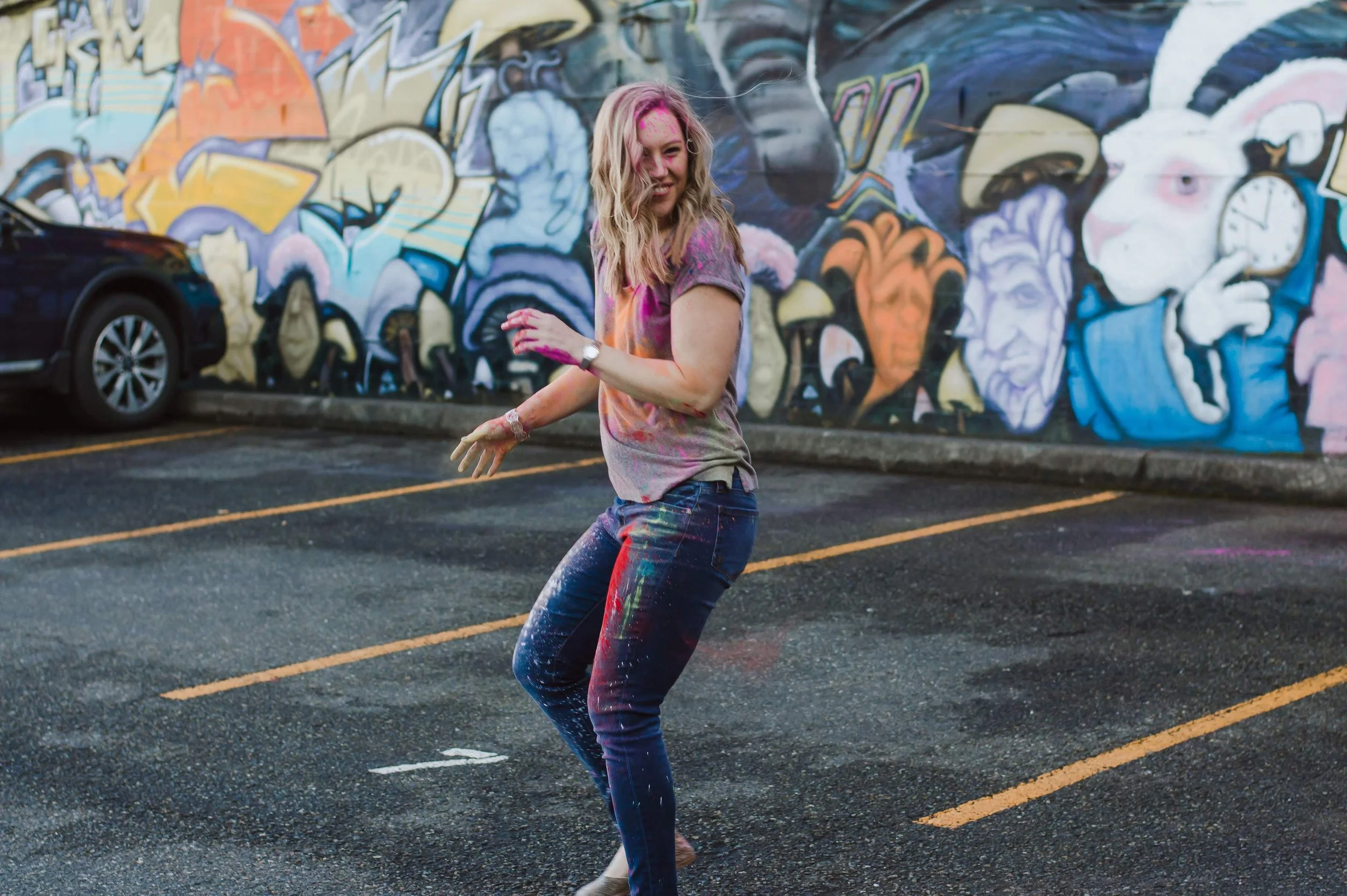 Mary Allison Jensen, LICSW, dancing joyfully covered in colorful powder paint in front of a vibrant mural — representing the energy and transformation inside The Self-Love Lab.