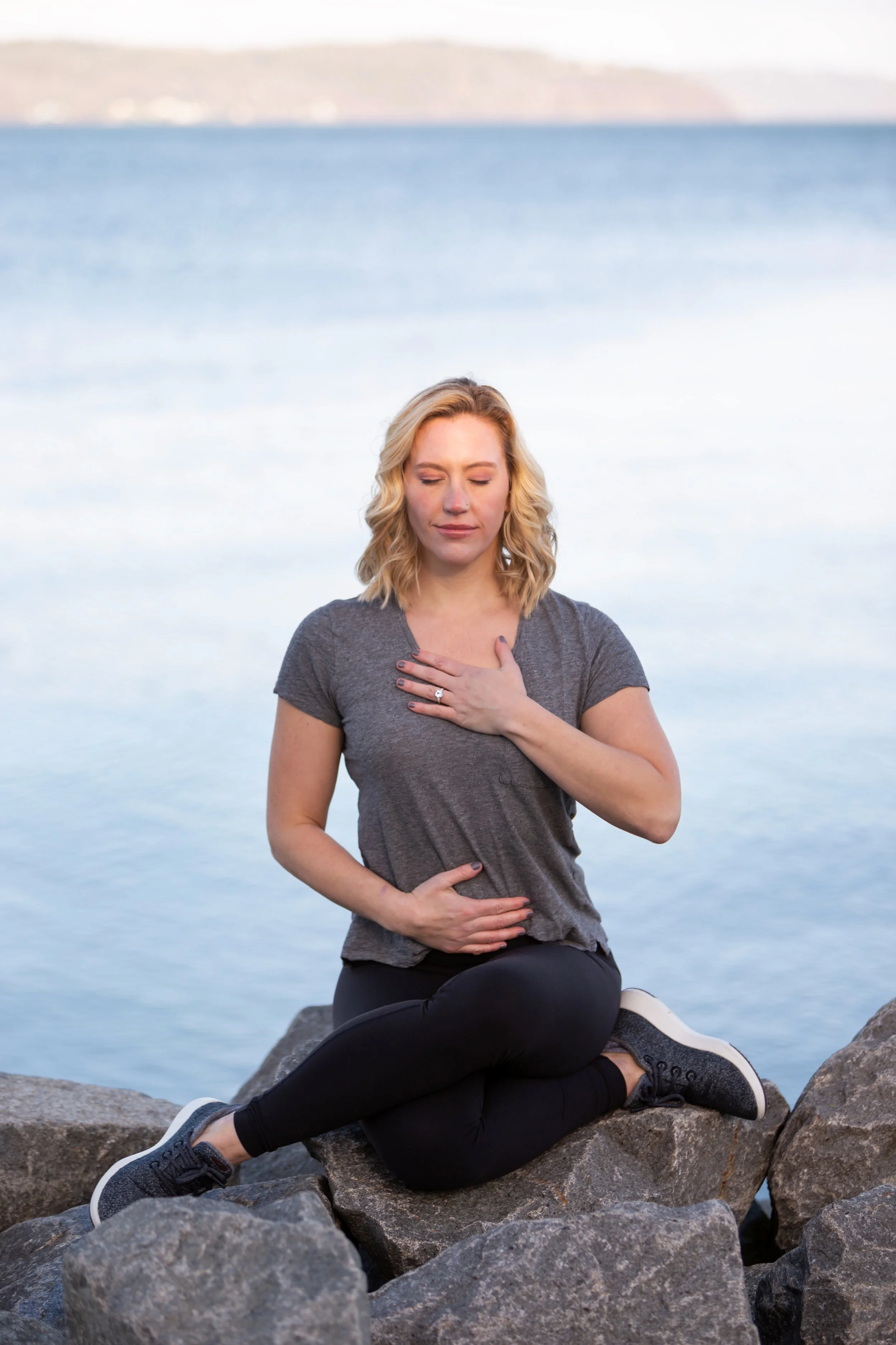Mary Allison Jensen, LICSW, sitting peacefully outdoors by the water with eyes closed and hands on her heart — embodying the somatic and belief work taught inside The Self-Love Lab.