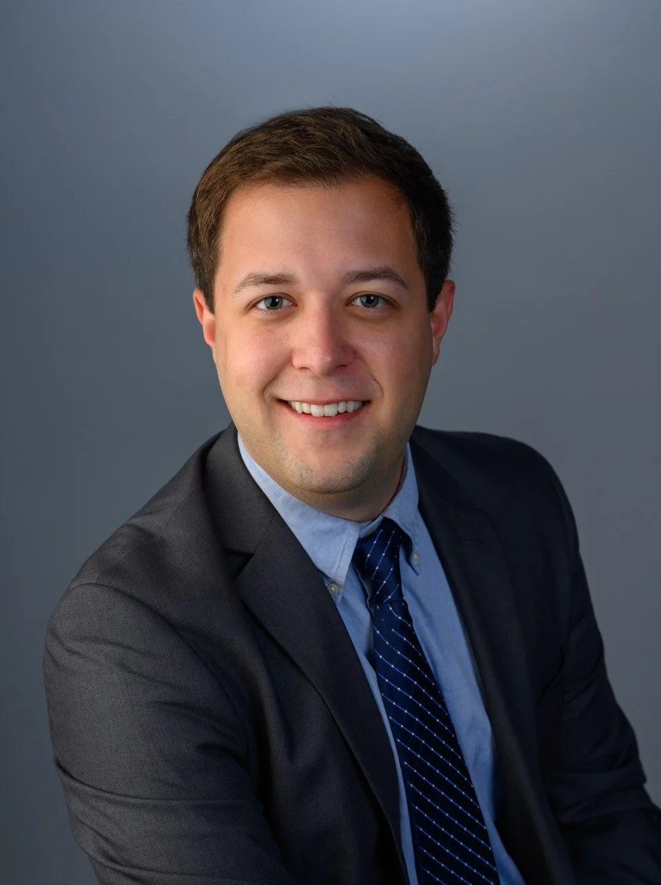 Portrait of Drew Bolog in a business suit and tie smiling against a plain gray background for 401(k) Audit Solutions.