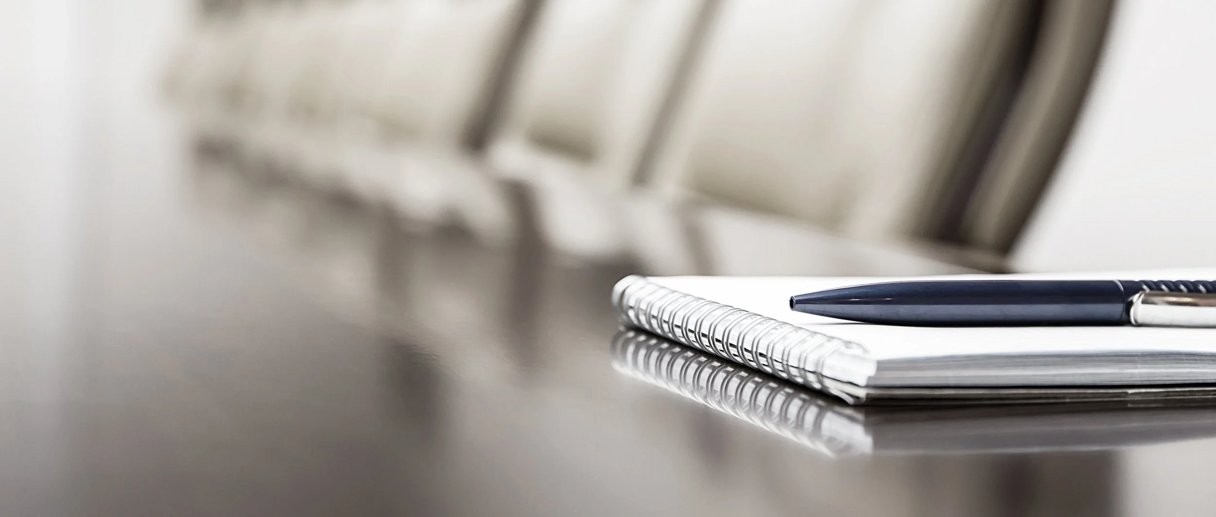 A black and silver pen resting on a closed spiral notebook, placed on a reflective surface with blurred background for 401(k) Audit Solutions.