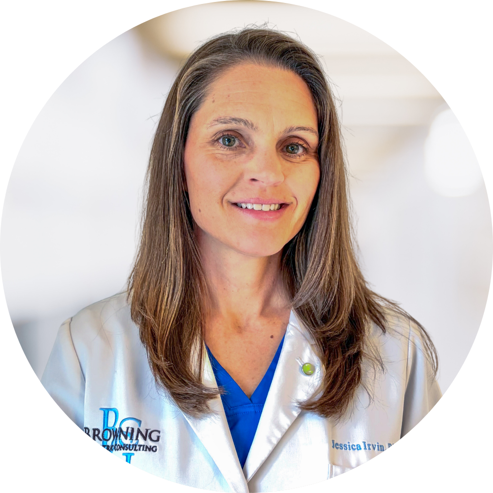 A woman wearing a white medical coat with a blue shirt underneath, smiling at the camera in a bright medical setting.