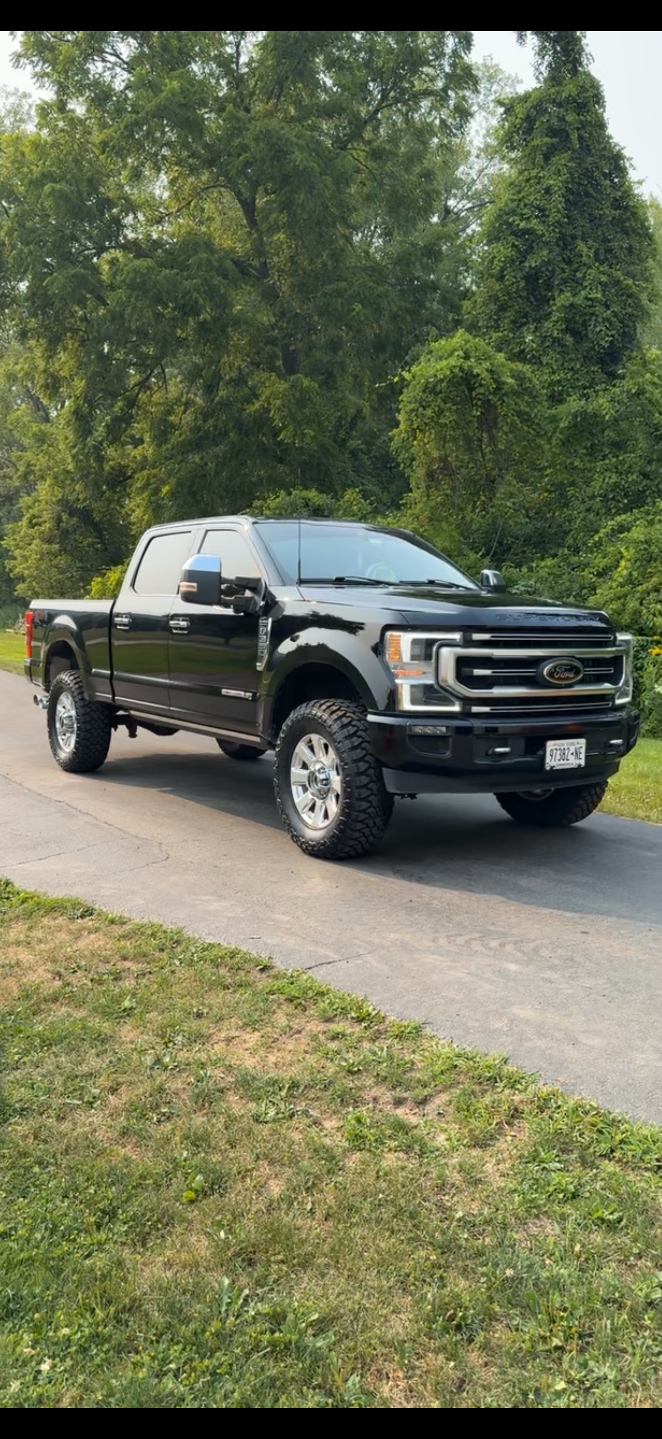 Black Ford F-150 pickup truck parked on a residential street with green trees and grass in the background.