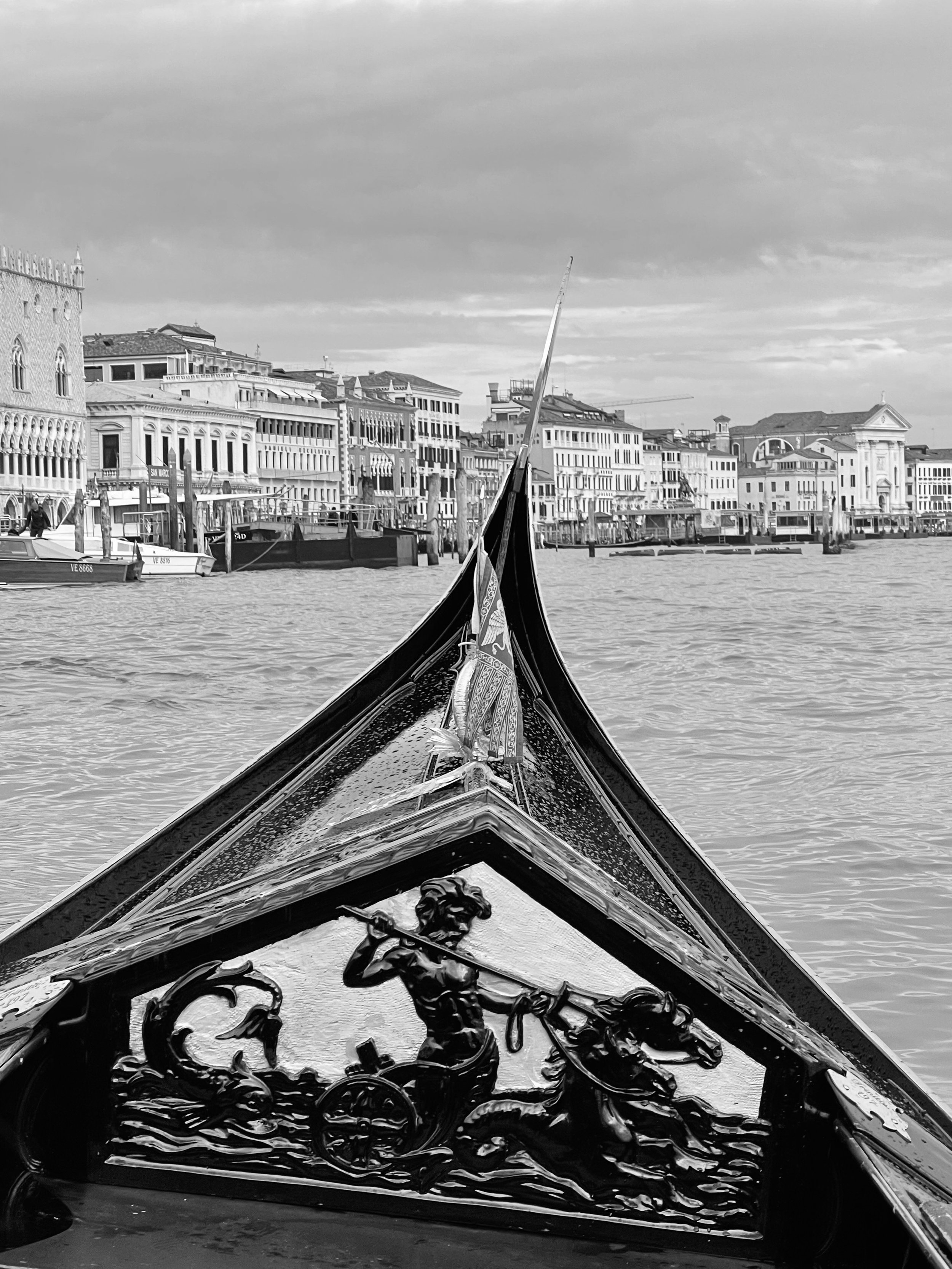 View from a gondola on a canal in Venice, Italy, with historic buildings lining the waterway and boats moored along the side.