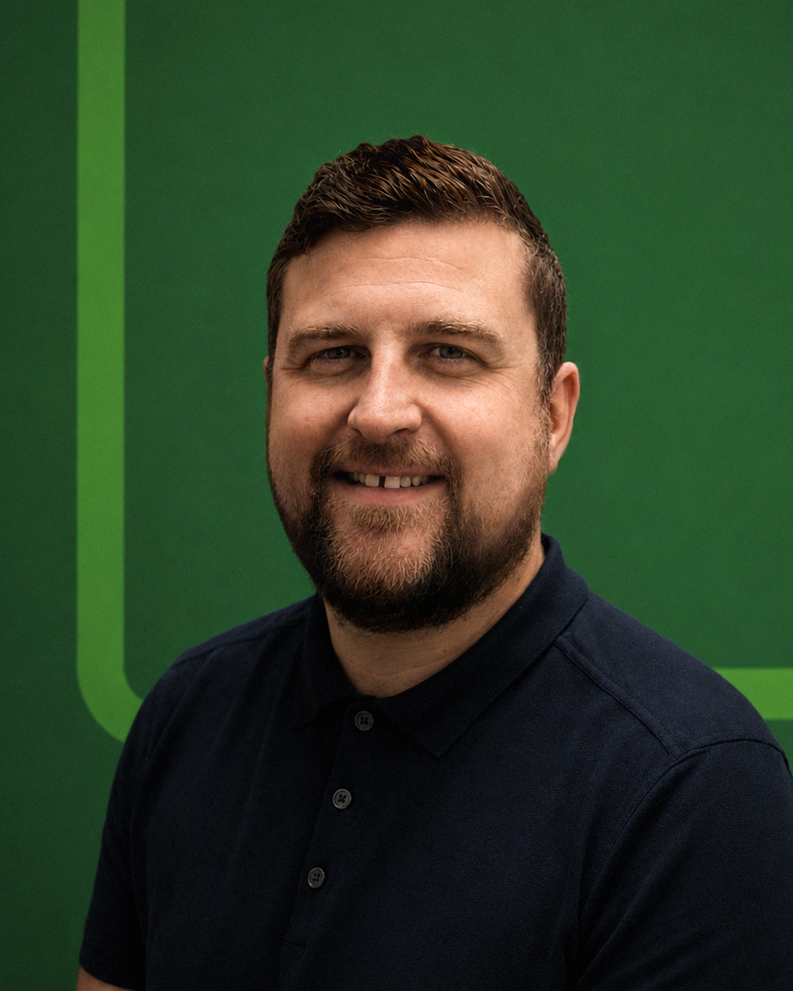 A smiling man with a beard and short hair stands against a green background.