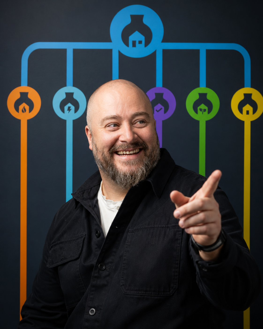 A smiling man with a beard wearing a black jacket and pointing with his right hand, standing in front of a dark wall with a colorful infographic featuring interconnected icons representing various scientific or technological concepts.