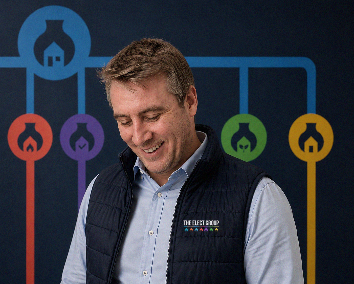 A man smiling in front of a graphic with interconnected icons of voting or decision-making processes, wearing a vest with the logo 'The Elect Group'.