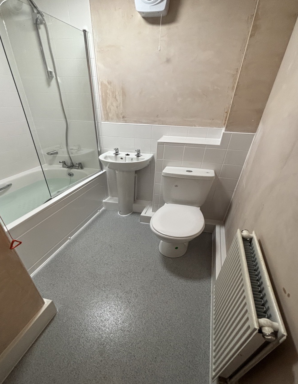 Bathroom with a bathtub and shower, a sink, a toilet, a radiator, and partially finished walls.