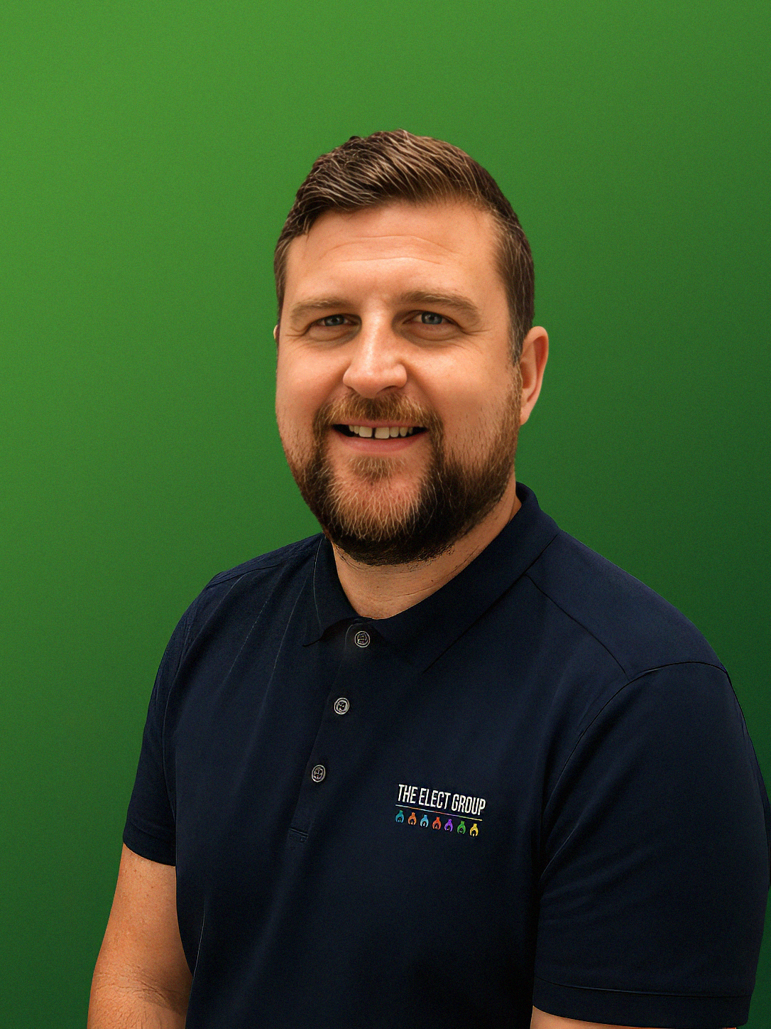 A smiling man with a beard and short hair stands against a green background.