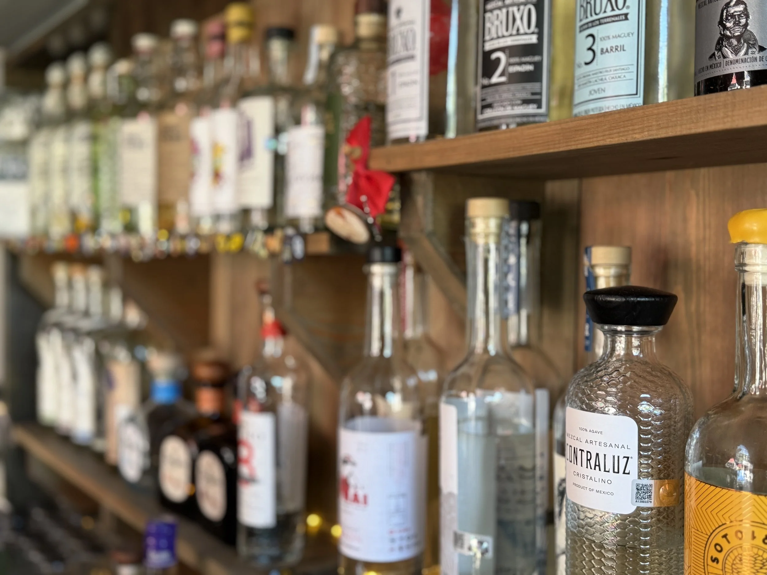 A wooden shelf filled with various bottles of alcohol, including tequila and other spirits, with labels showing different brands and types.
