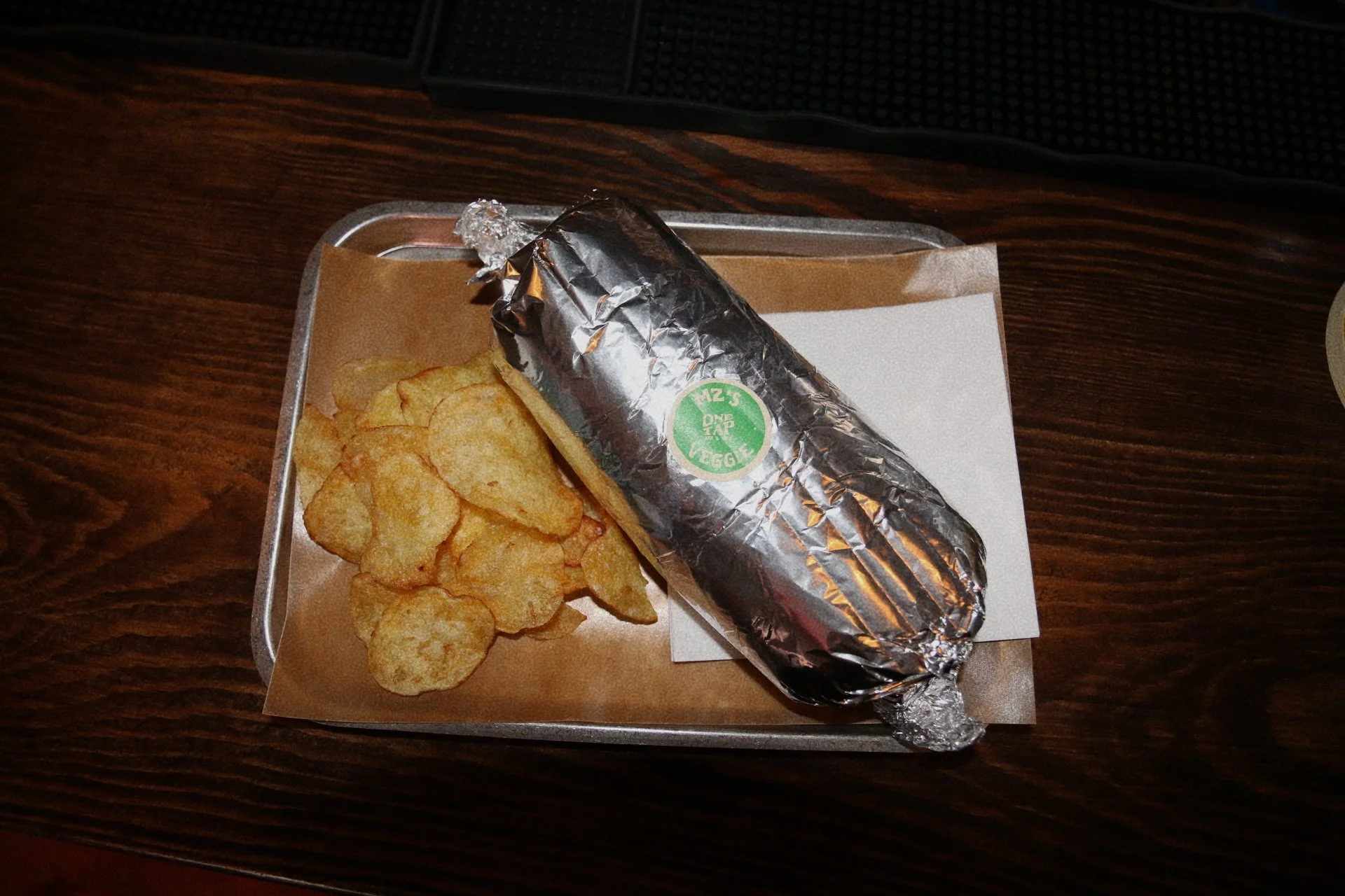 A tray with potato chips and a wrapped burrito on a dark wooden table.