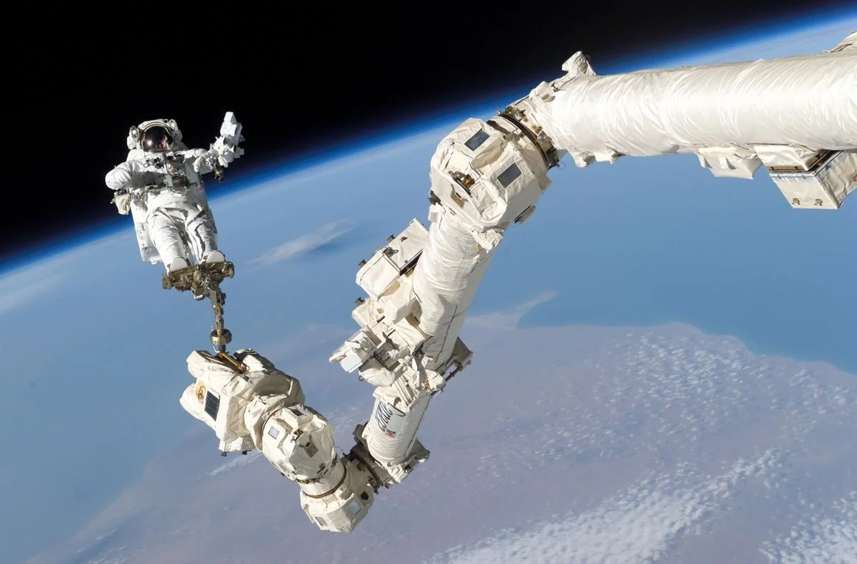 An astronaut performs an extravehicular activity with the International Space Station floating in the background over Earth.