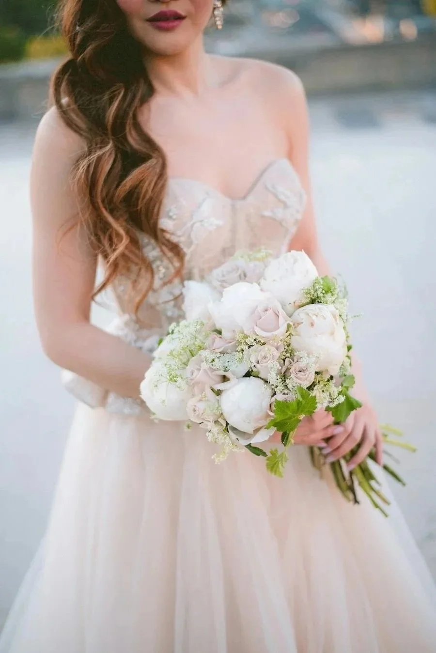 A woman in a wedding dress holding a bouquet of white and pale pink flowers.