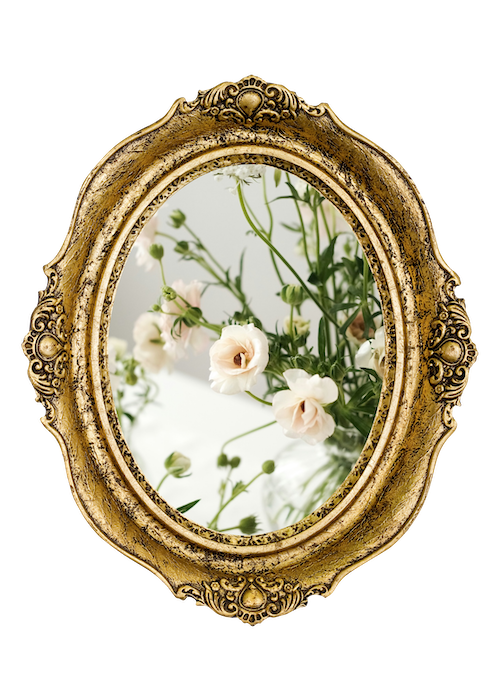 Vintage ornate gold oval mirror reflecting white and light pink flowers on green stems