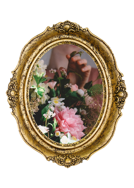 Reflection of a person taking a photo of a floral bouquet in an ornate gold oval mirror.