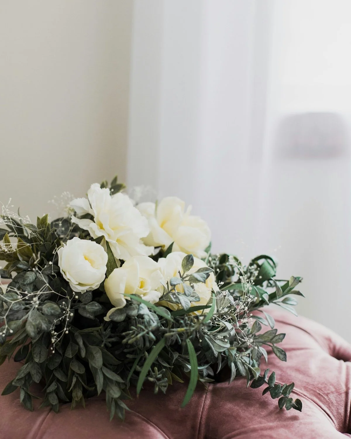 A bouquet of white and cream flowers with green foliage resting on a pink cushion.