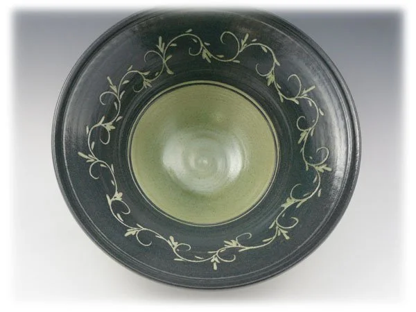 Top view of a dark glass bowl with a decorative white vine pattern around the rim and a greenish-yellow interior.