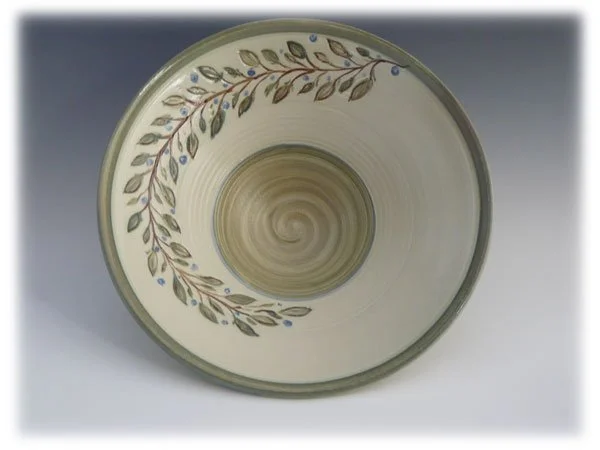 Top view of a ceramic bowl with a decorative pattern of leaves and small blue berries around the rim, viewed from above.