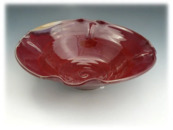 A red and yellow glass bowl with a swirling pattern inside, placed on a plain surface.