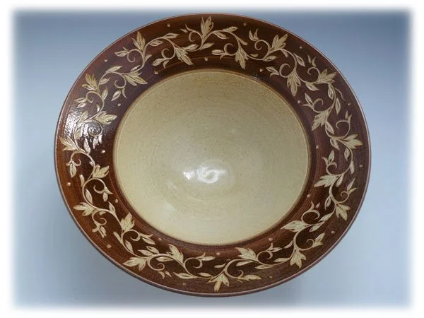 A ceramic bowl with a brown exterior and beige interior, decorated with a beige leafy vine pattern on the rim.