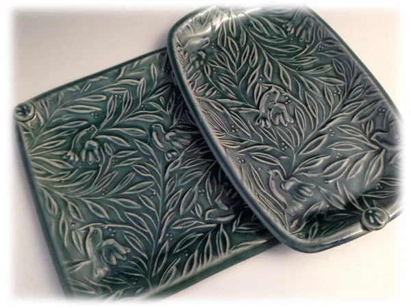 Two small dark green rectangular boxes with intricate floral and leaf patterns embossed on their lids, one slightly open.