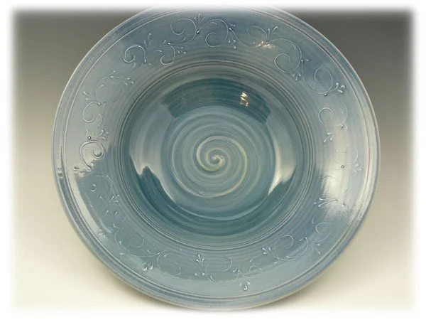 A clear glass bowl with a decorative swirling pattern around the rim, containing a spiral liquid with a swirled design.