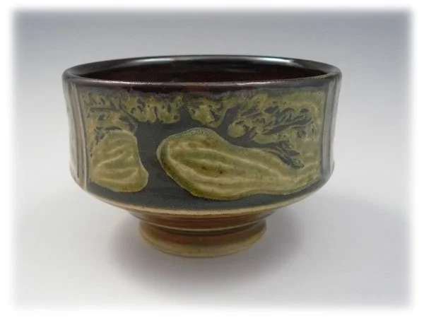 A ceramic bowl with a black background and artistic greenish-yellow swirl designs on the exterior, placed on a white surface.