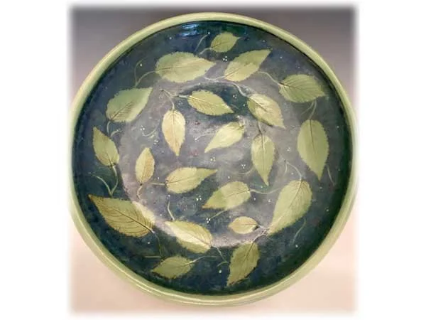 A round bonsai watering dish with floating green and yellow leaves.