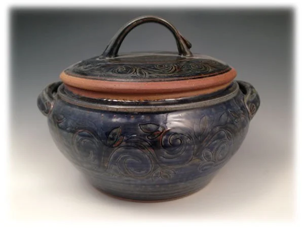 A ceramic pot with a lid and handle, decorated with swirling patterns in dark blue and black, and a terracotta-colored accent around the lid.