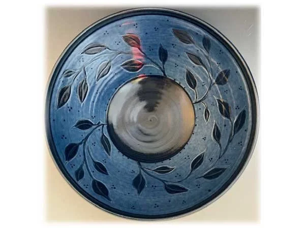 Top view of a glass bowl with a blue background and leaf patterns engraved on the inner surface.