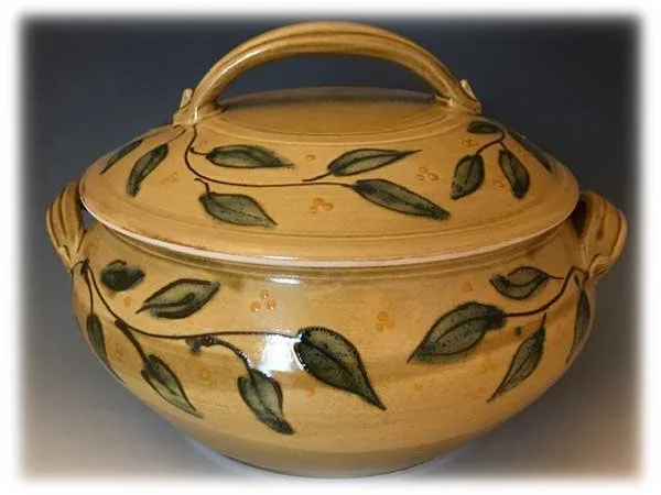 A round ceramic soup tureen with a lid and a handle, decorated with green leaves and small yellow flowers.