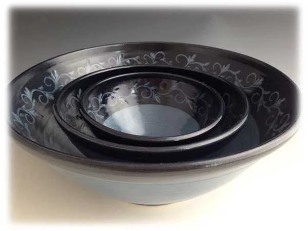 Three nested black bowls with decorative white floral patterns inside, placed on a white surface.