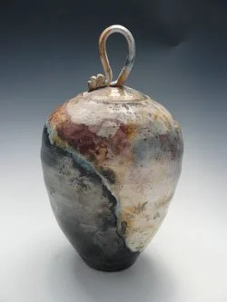 A ceramic vase with a weathered glaze, featuring a metal handle at the top.