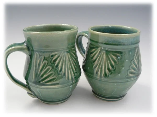 Two green ceramic mugs with decorative leaf and dot patterns, side by side on a white background.