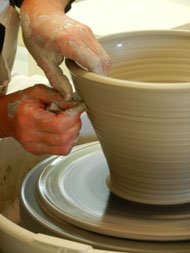 A person’s hands shaping a ceramic bowl on a pottery wheel.