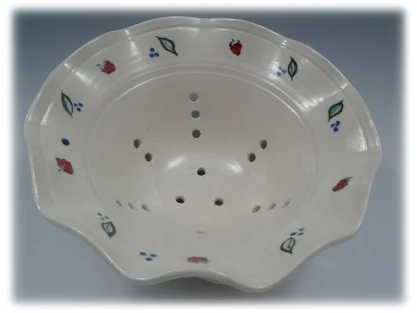White ceramic colander with floral and leaf patterns around the rim, holes for draining, and a scalloped edge.