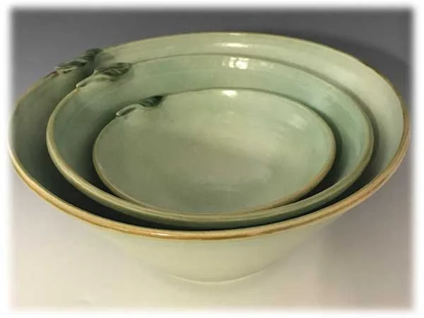 Set of three green ceramic bowls of different sizes stacked inside each other with a plain background.