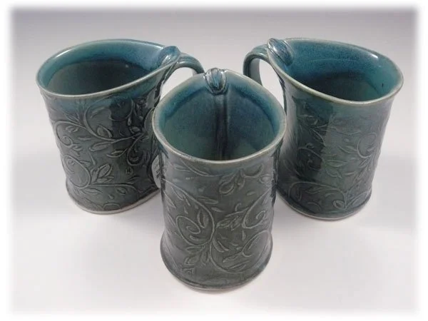 Three ceramic mugs with a floral pattern, filled with dark liquid, placed on a white surface.