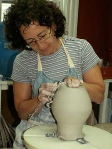 Woman shaping a ceramic vase on a pottery wheel in a studio