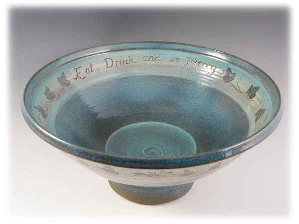 A decorative blue ceramic bowl with a quote "Eat, Drink and be Merry" and floral designs around the rim.