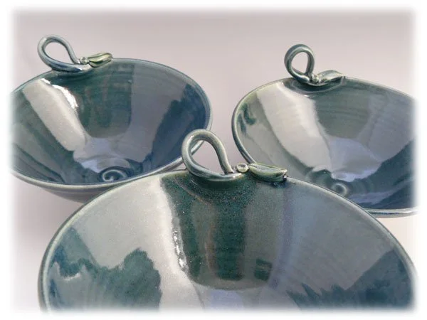 Three glossy ceramic bowls with metal loops for hanging, arranged with one in front and two behind, on a white surface.