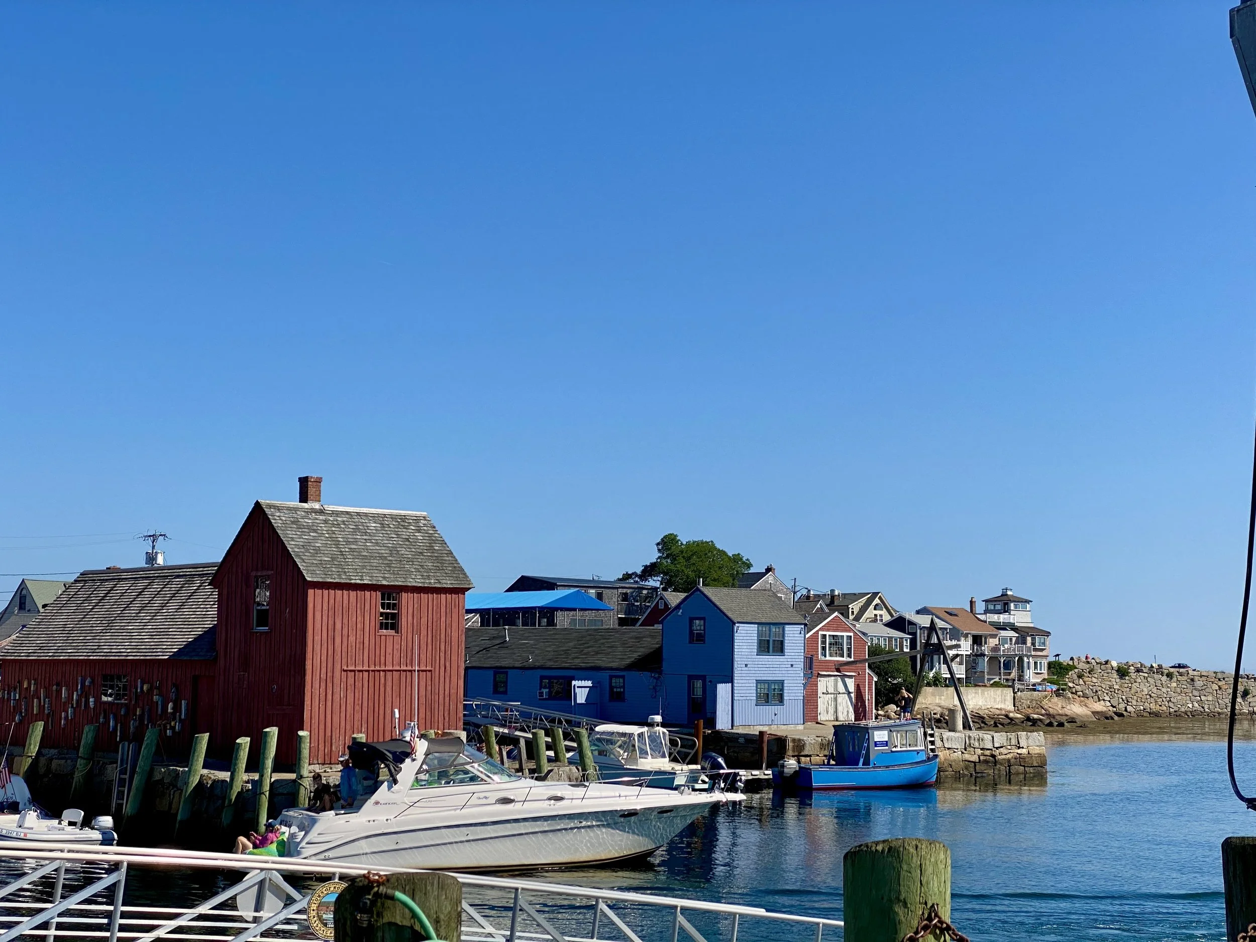 A harbor with boats docked near colorful buildings, including a red wooden house, under a clear blue sky.
