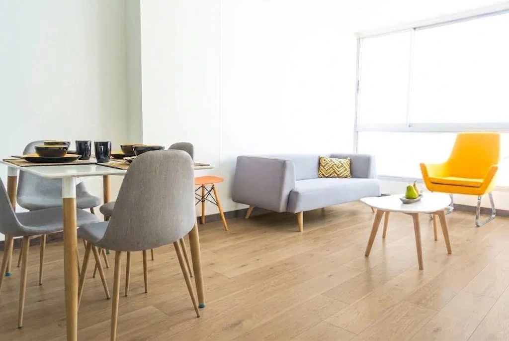 Sala de estar con grande ventana, cortinas oscuras, planta en maceta, sillón, y decoración con cuadros y jarrón.