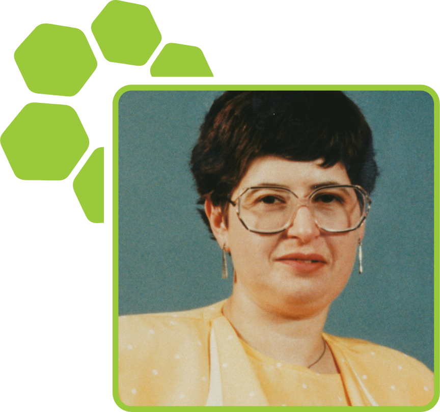 A woman with short dark hair, glasses, earrings, and wearing a yellow outfit against a blue background.