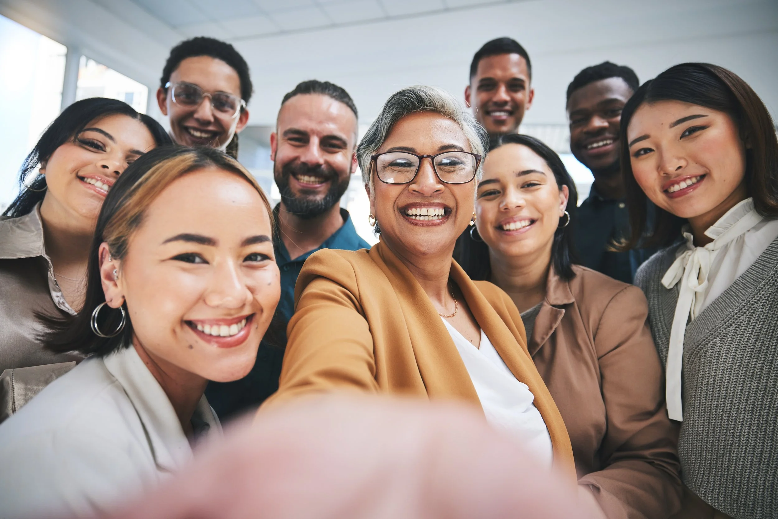 A diverse group of ten smiling people taking a selfie together in an indoor setting.