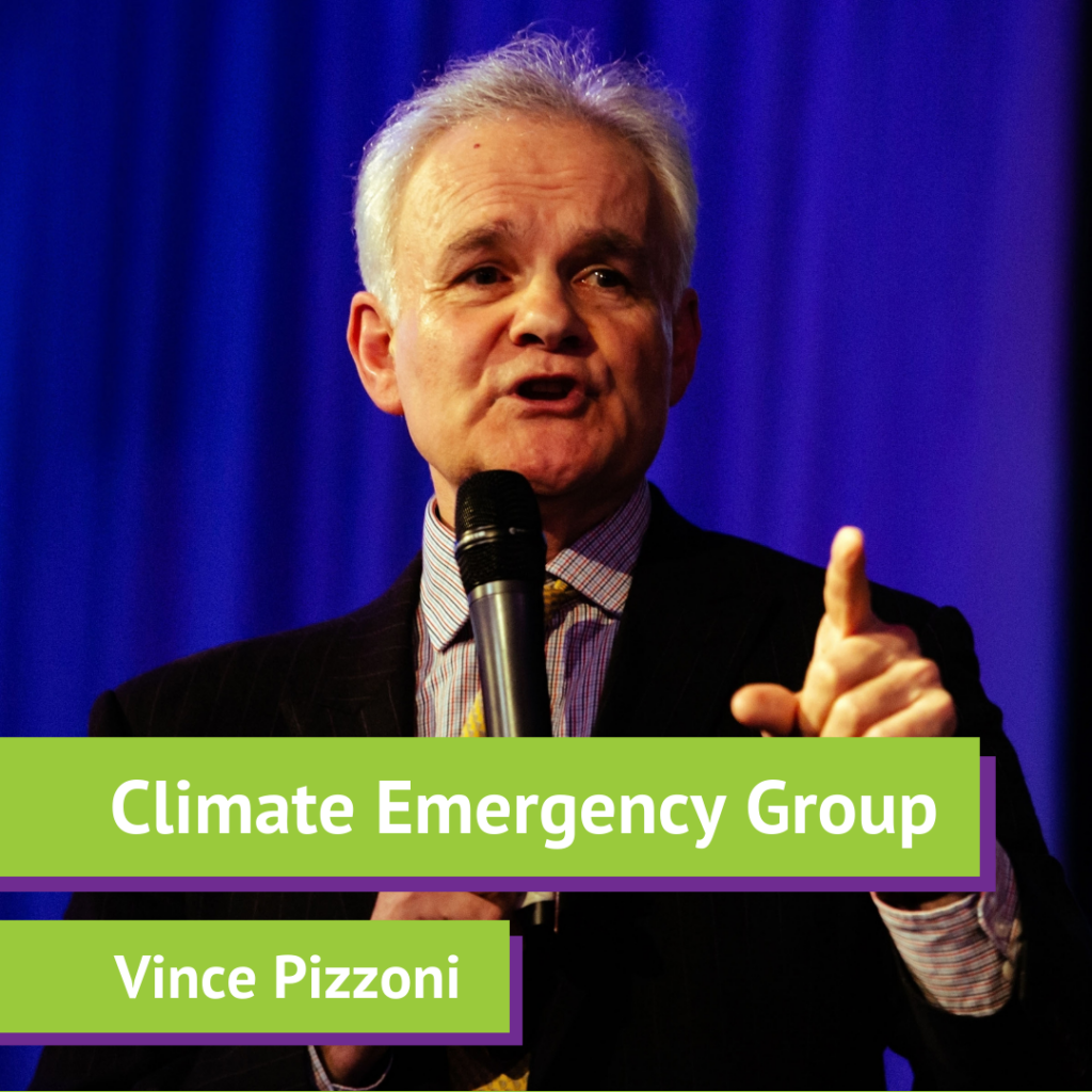 A man with white hair speaking into a microphone on stage, gesturing with his right hand, with a blue curtain background. The lower third of the image has green and purple labels that read 'Climate Emergency Group' and 'Vince Pizzoni'.