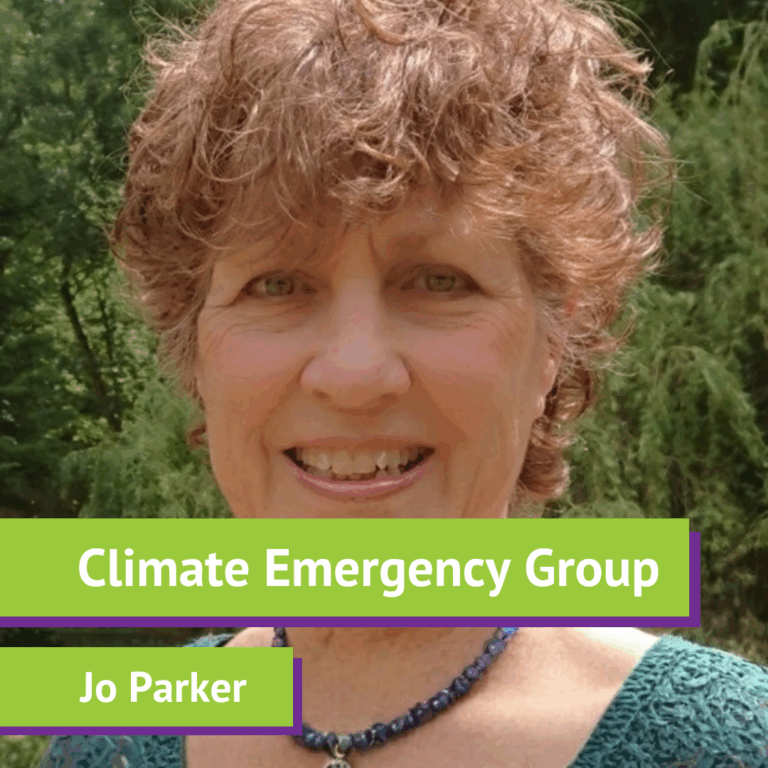 A woman smiling outdoors with green trees in the background, wearing a dark top and a beaded necklace. There is a green and purple banner across the bottom with the text 'Climate Emergency Group' and 'Jo Parker.'